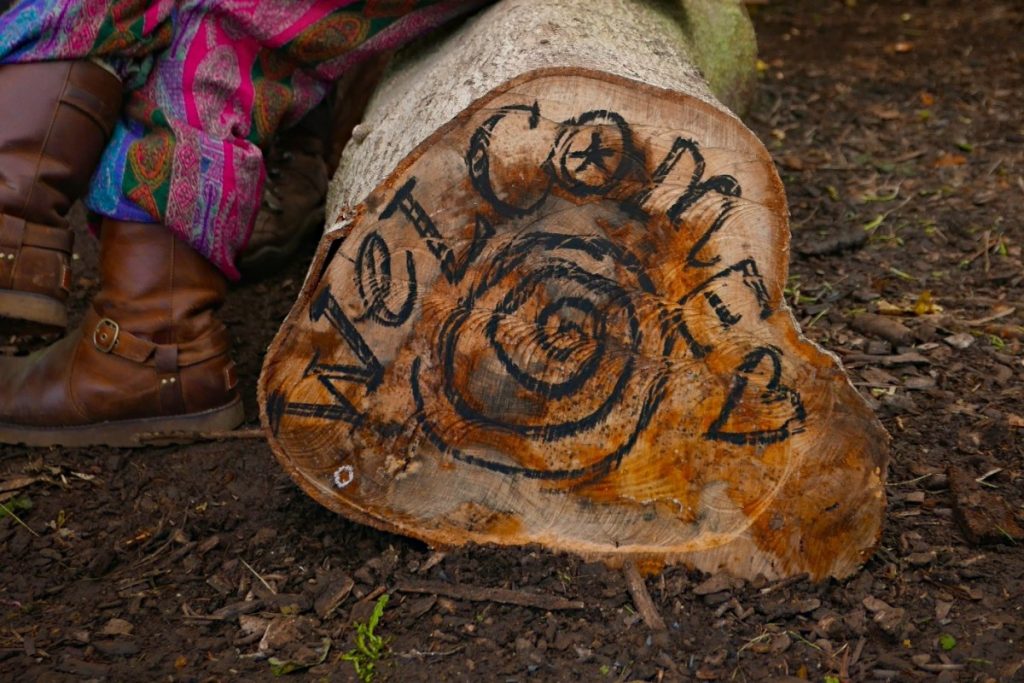 A log with welcome written on the side and a person sitting on it